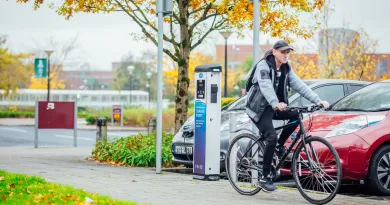 Male student cycling past a car park on campus.