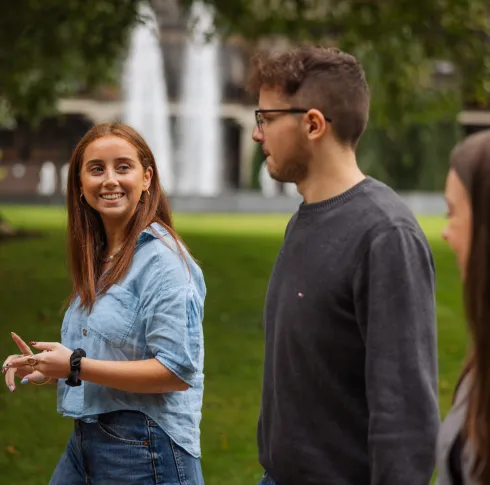 3 Students walking and talking past a fountain