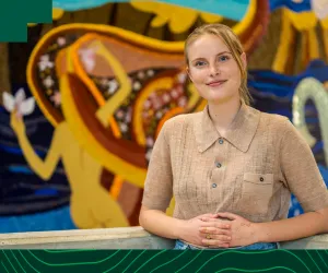 Woman in brown shirt stands in front of arts image 