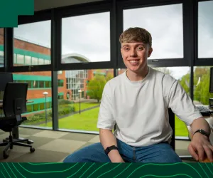 business student wearing white top sits with window behind him 
