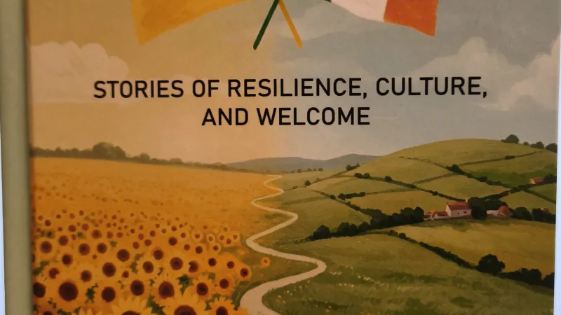Front cover of book titled "our new friends from ukraine to ireland" including the irish and ukranian flags over a green field and a field with sunflowers. Path between the two fields with two figures walking.
