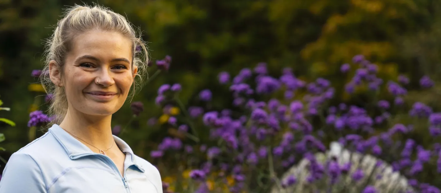 Blonde girl with light blue top smiling in front of wild irish flowers
