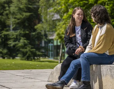 two students sitting outside on a stone chatting 