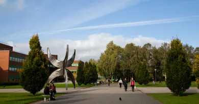 View from KBS of statue outside Schumann Building with people walking in front and trees in the background. 