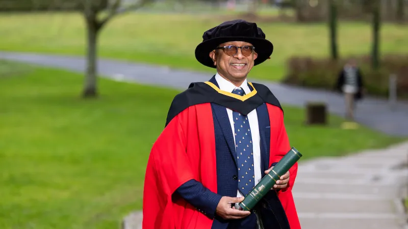 Professor Roy Philip in PhD graduation robes holding scroll