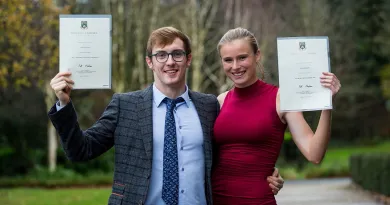 a man and a woman smiling and holding up their UL degrees